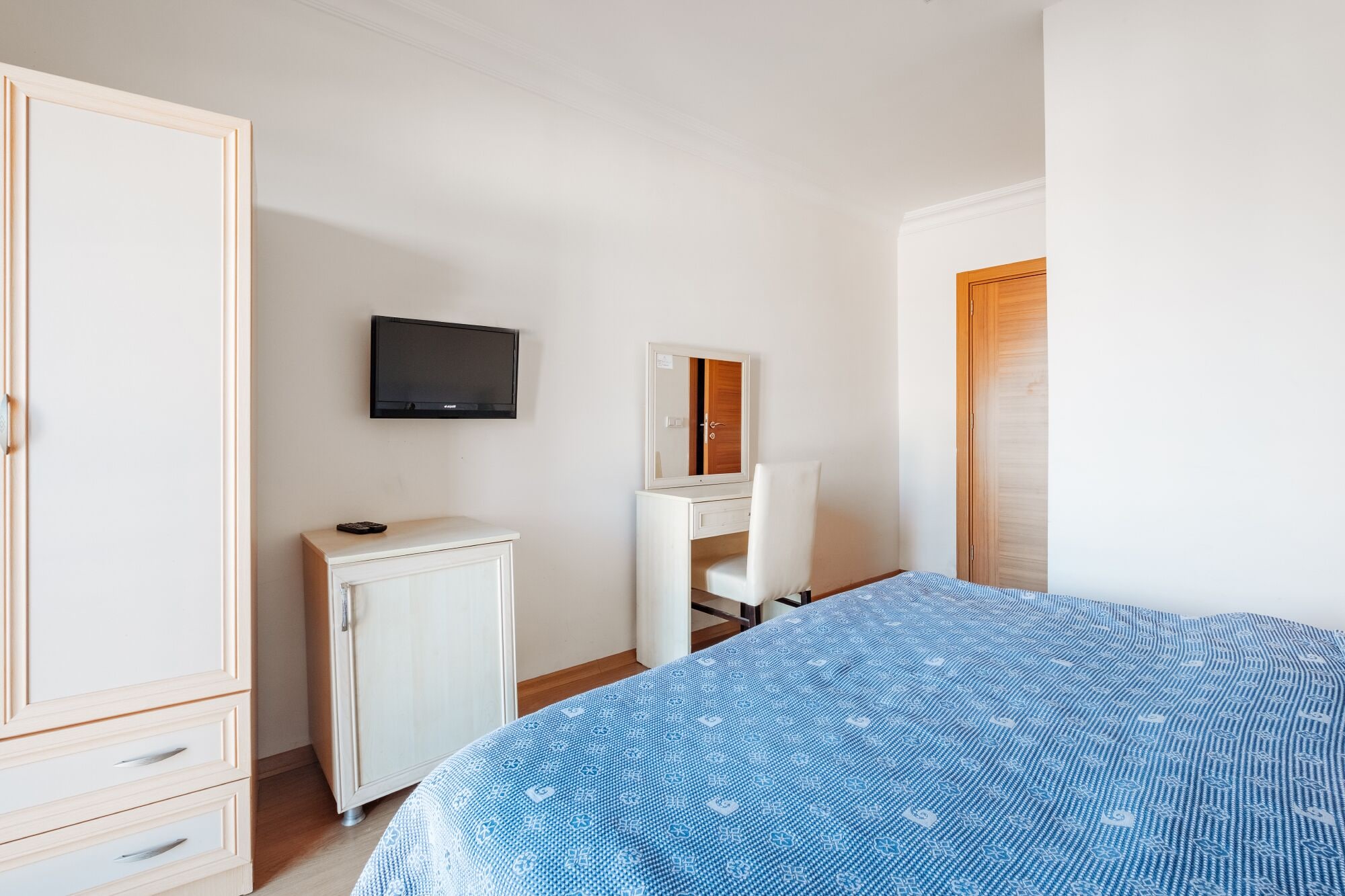 A bedroom with a bed, a wardrobe, a desk, a mirror, and a television.