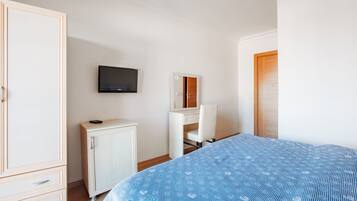 A bedroom with a bed, a wardrobe, a desk, a mirror, and a television.