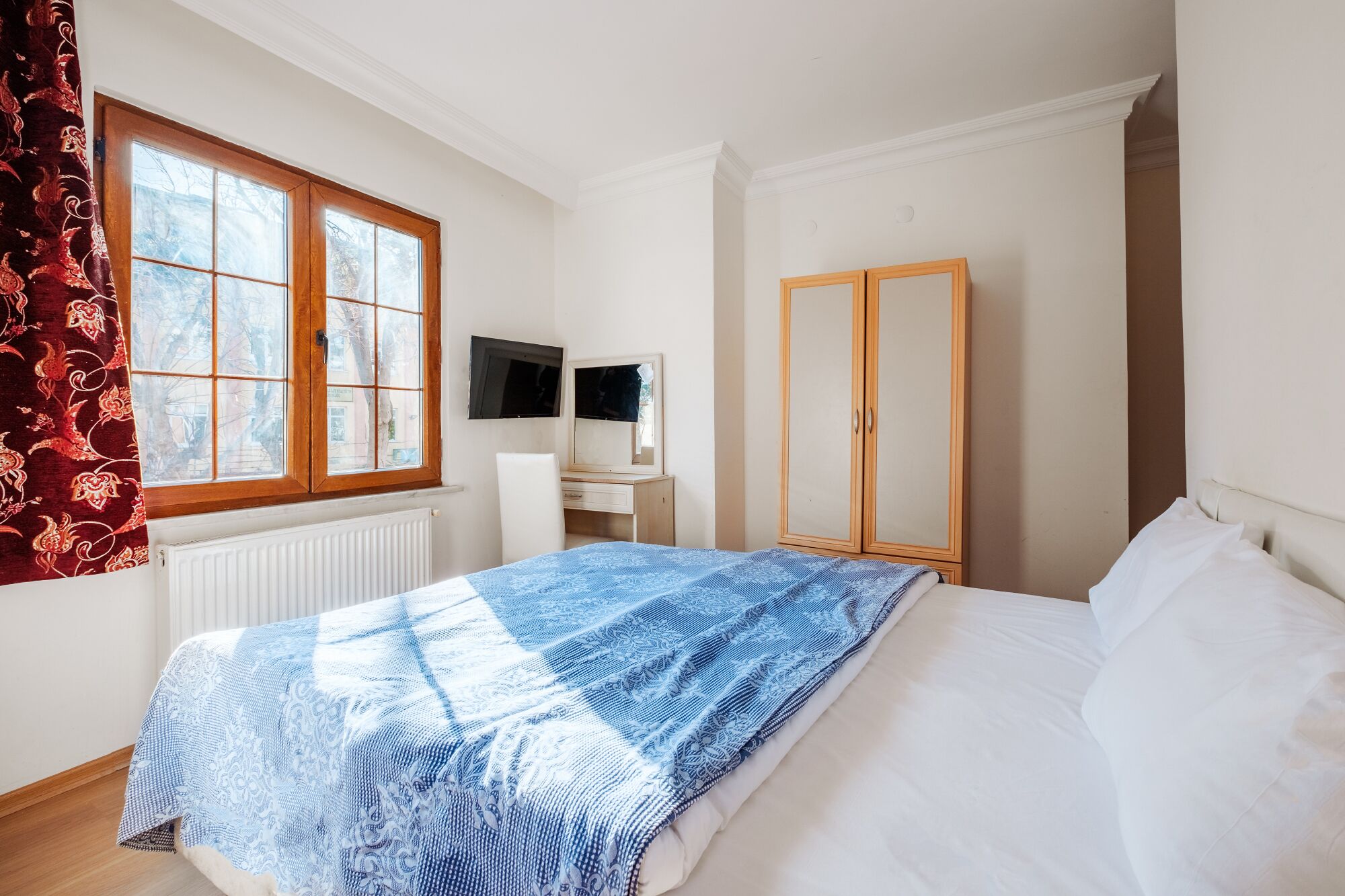 Un dormitorio con cama, escritorio con silla, armario y ventana con cortinas.