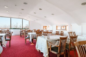 Ein Essbereich mit Tischen, Stühlen, großen Fenstern und einem roten Teppich.