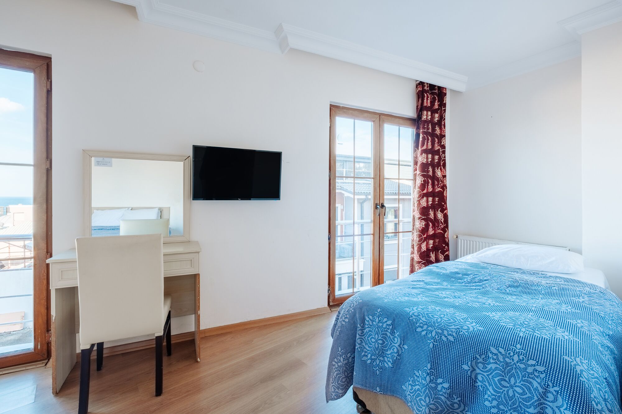 Une chambre d’hôtel comprenant un lit, un bureau avec une chaise, un téléviseur fixé au mur et une fenêtre donnant sur des immeubles.