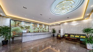 Un vestíbulo de hotel con mostrador de recepción, zona de estar con sofás, candelabro y un mural grande en la pared.