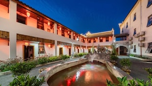 Un patio central con una fuente, rodeado de edificios tradicionales con varios balcones e iluminación cálida.