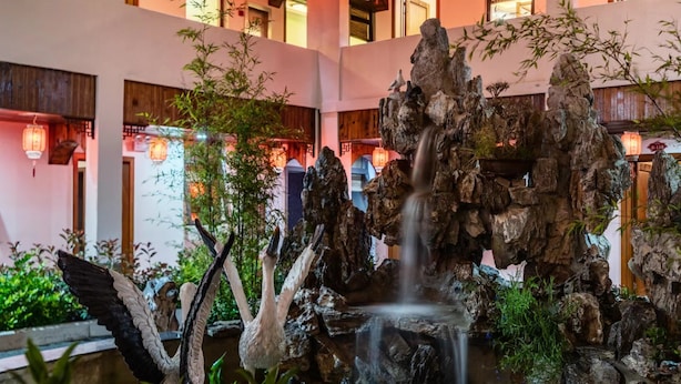 Un jardín interior tranquilo con cascada, bambú y una escultura de ave.