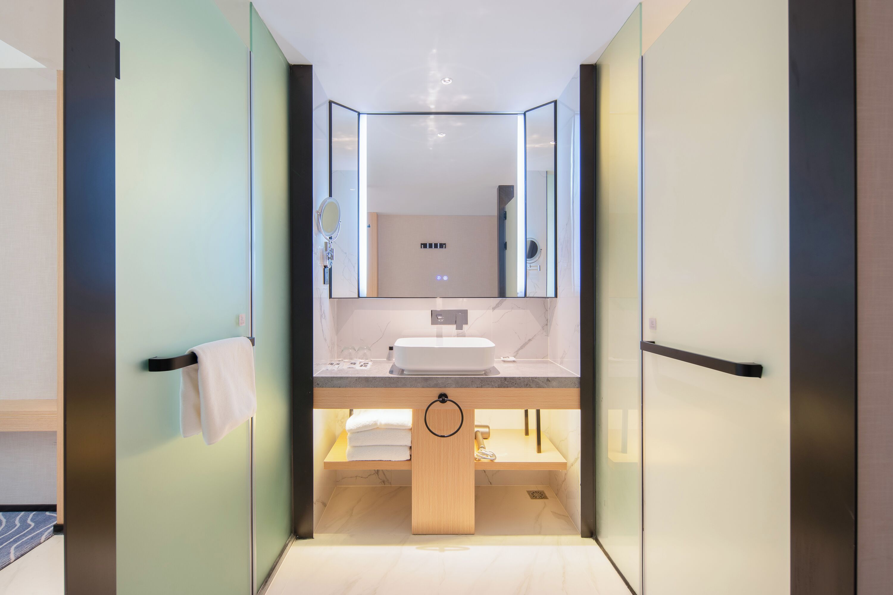 A modern bathroom with a large mirror, a sink, and a towel rack.