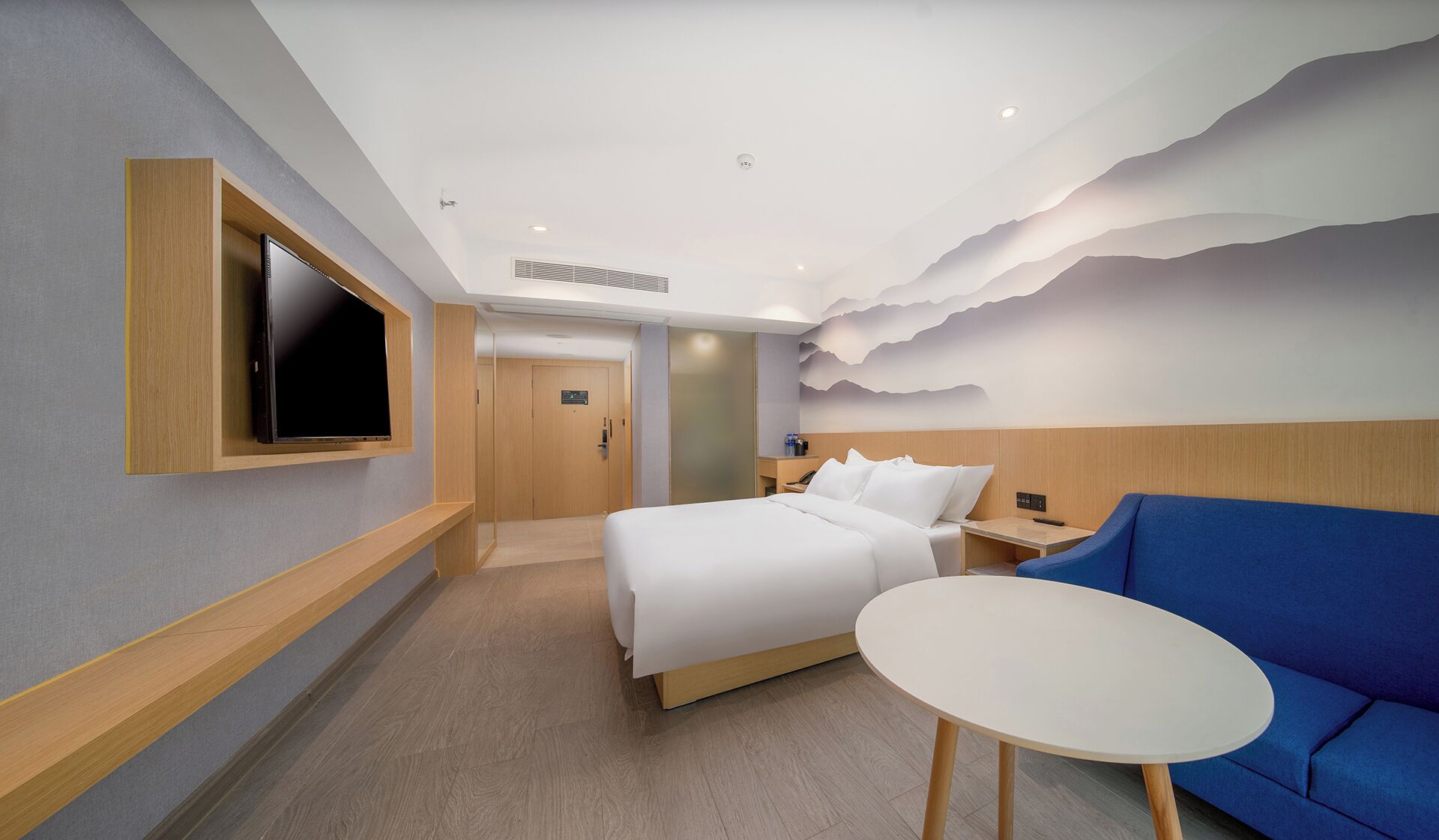 A hotel room with a bed, a TV mounted on the wall, a blue sofa, and a small table.