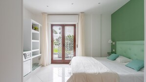 Een moderne slaapkamer met een groot bed, een groene accentmuur, een inbouwkast en een schuifdeur van glas die leidt naar een buitenruimte.