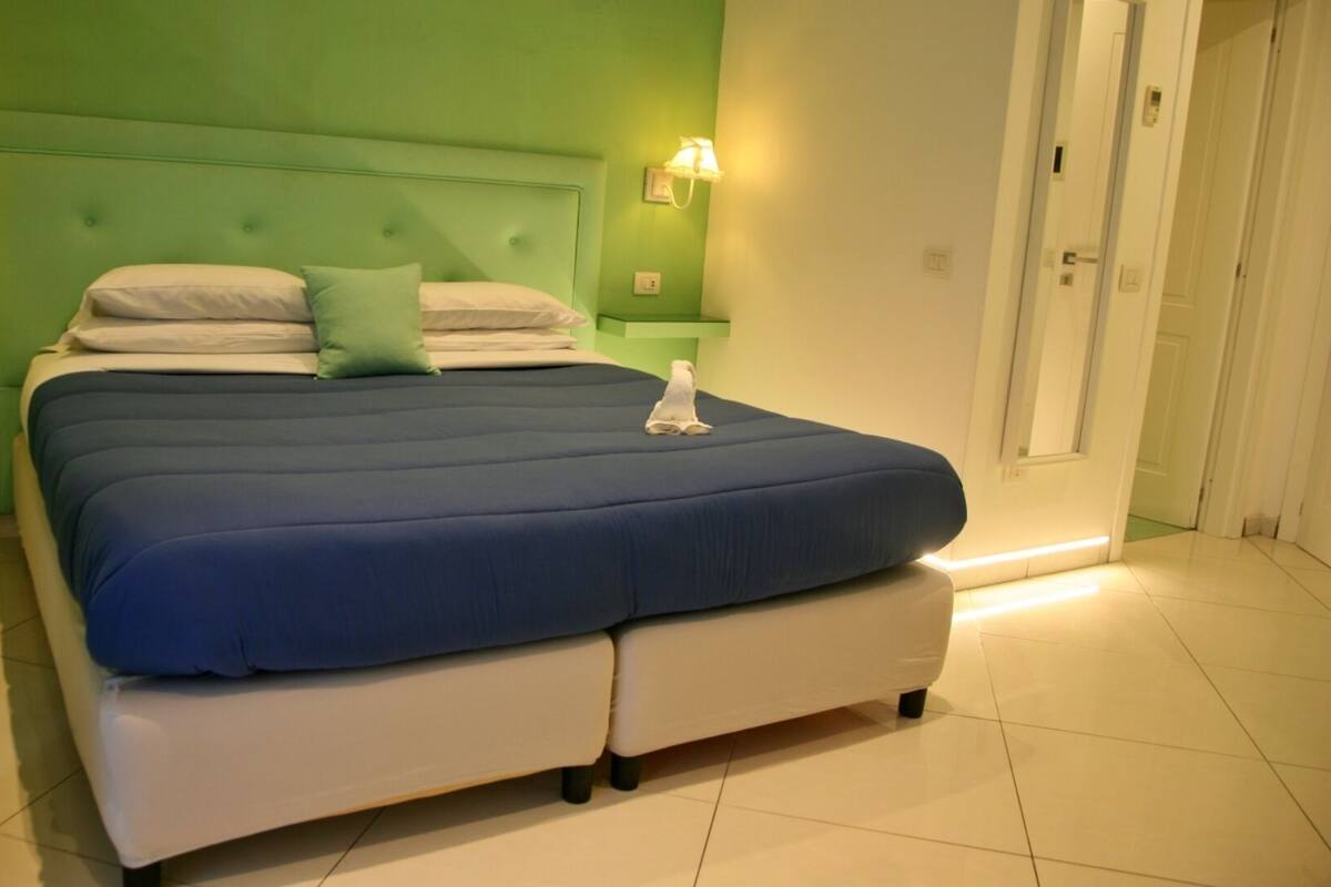 Een bed met een blauwe matras, een wit hoofdbord, twee kussens en een witte deken.
