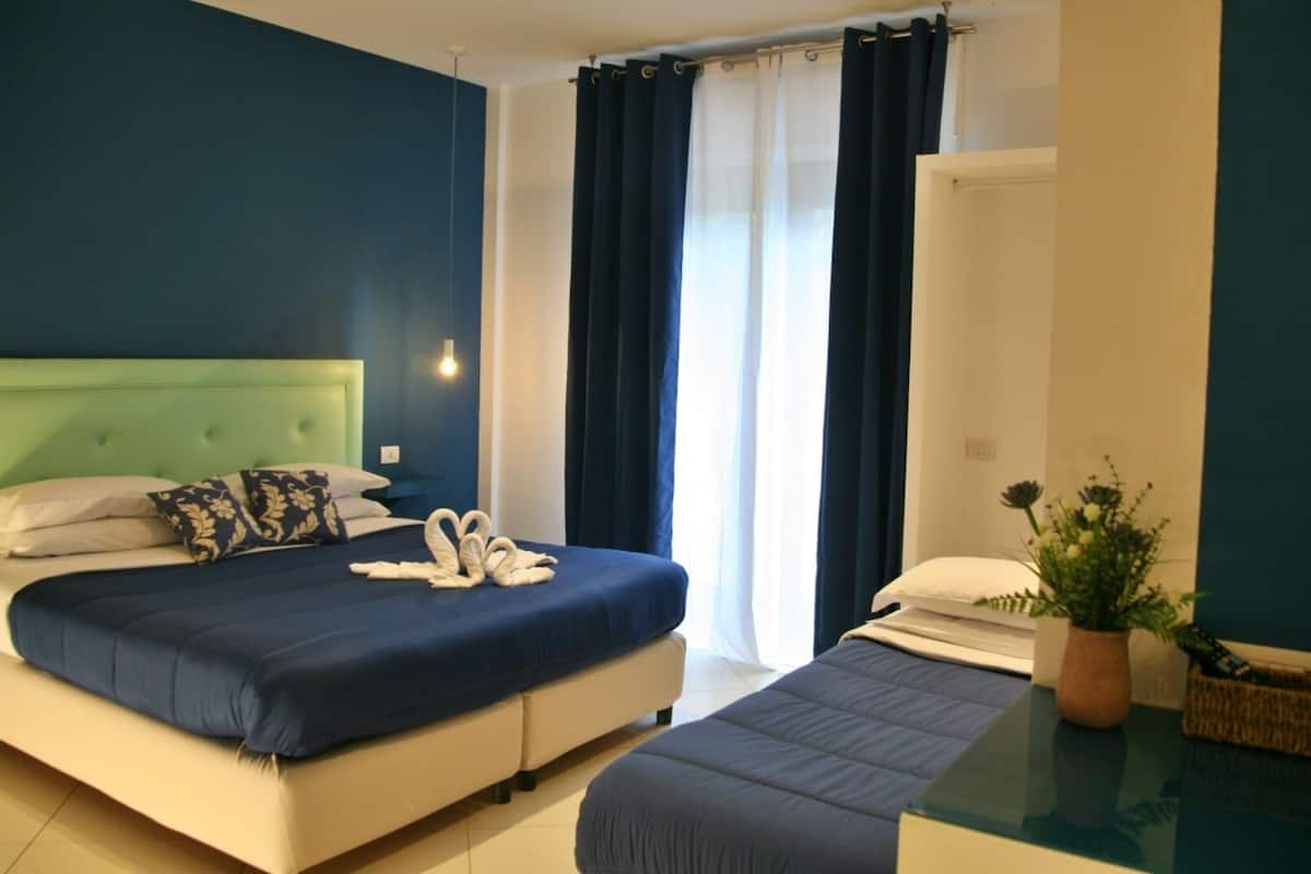 Een hotelkamer met een bed, een bankje, een plant in pot en een douchehoek.