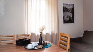 A dining area with a wooden table, two chairs, a black tray with cups and snacks, a vase with dried flowers, and a framed picture on the wall.