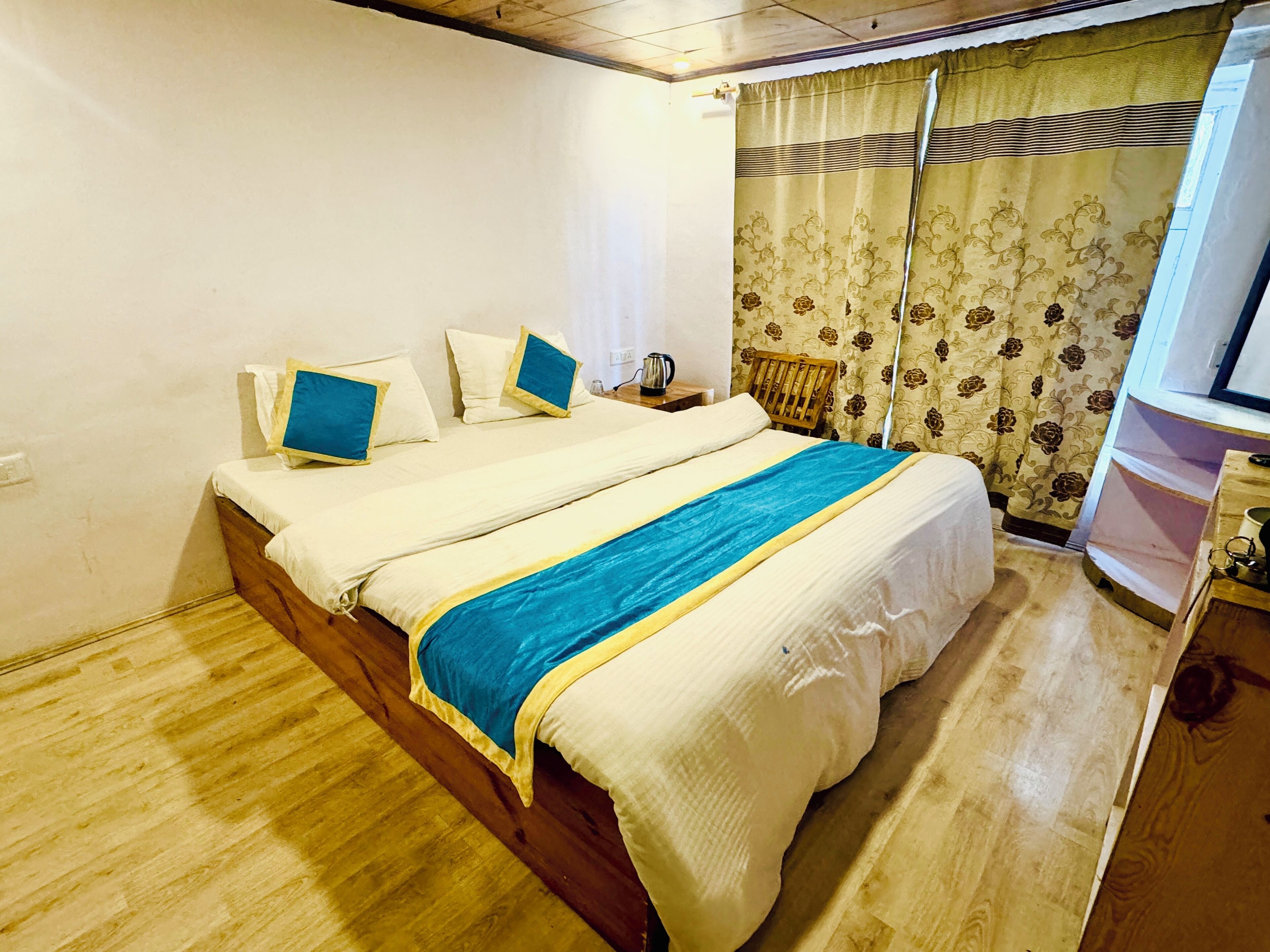 Een tweepersoonsbed met een blauw-gele sprei, witte kussens en een houten hoofdbord.