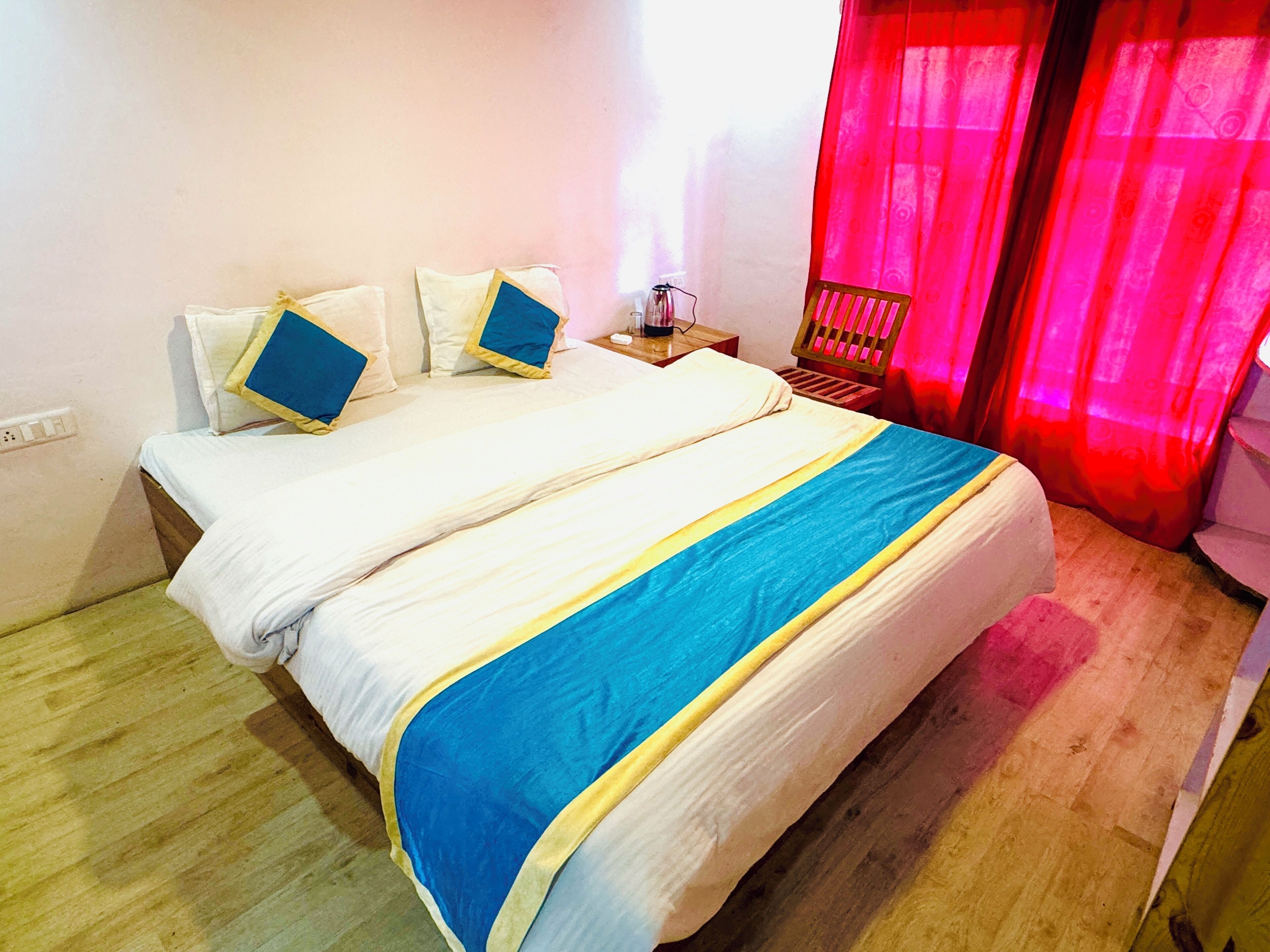 A double bed with a blue and yellow bedspread, white pillows, and a wooden nightstand with a lamp.