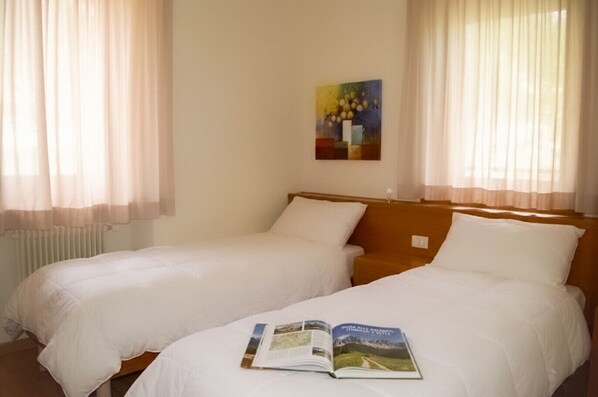 Hotellihuone, jossa on kaksi erillistä sänkyä, puinen pääty, patteri ja taulu seinällä.