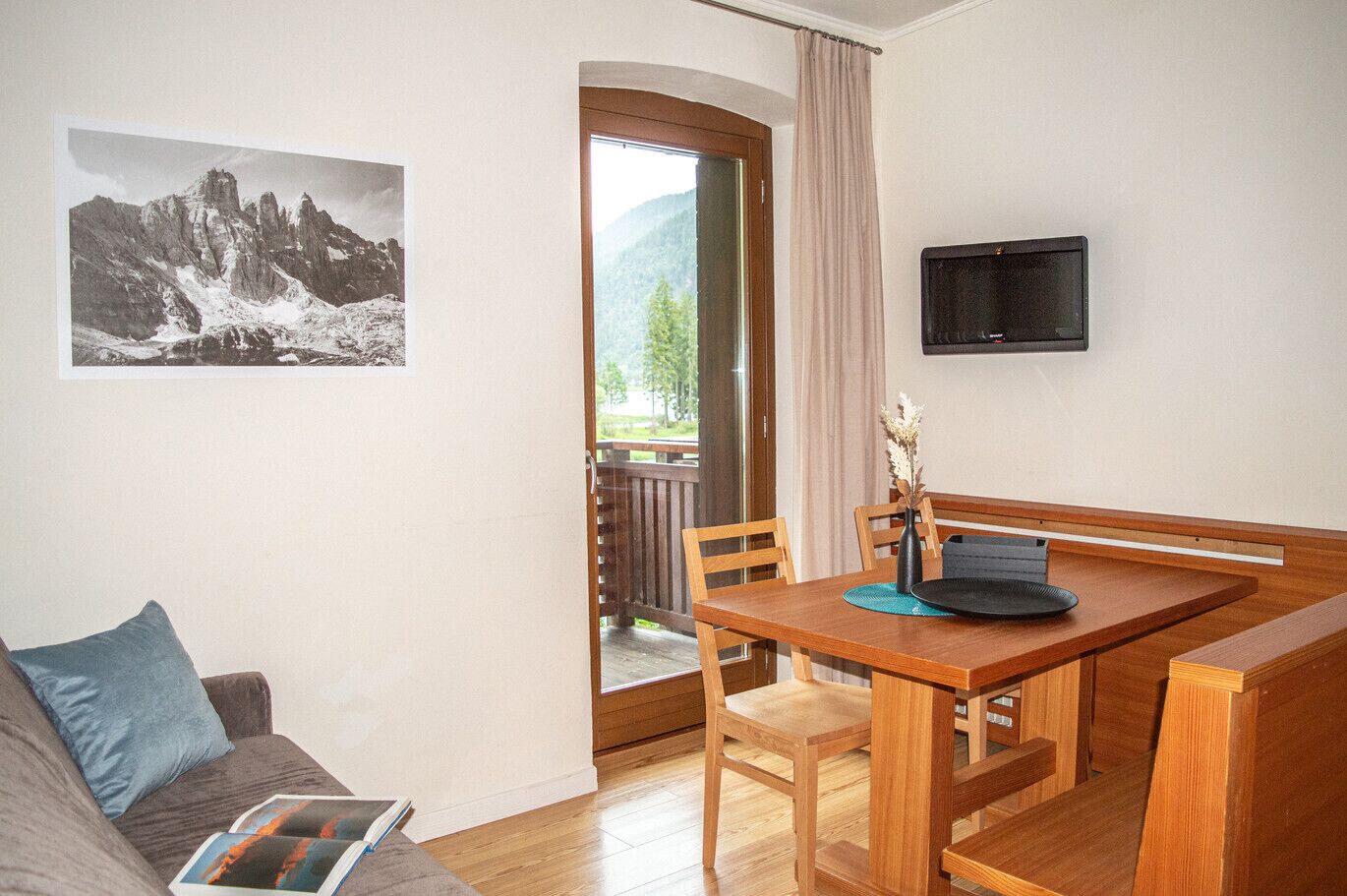 Una habitación con una mesa de comedor de madera, sillas, un televisor montado en la pared, un ventanal con vistas a montañas y una puerta que da al exterior.