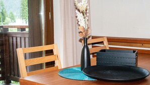A dining table with a black plate, a vase with dried flowers, and a wooden chair.