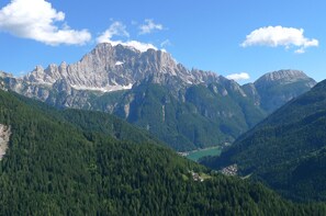 A mountainous landscape with a prominent rocky peak, dense forested valleys, and a small settlement in the valley.