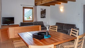 Ein gemütlicher Wohnbereich mit einem Holzesstisch, Sofas, einem Fernseher und einem Fenster mit Bergblick.