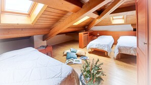 Ein Schlafzimmer im Loft-Stil mit Holzbalken, Dachfenstern und zwei Betten.