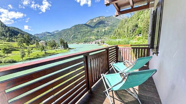 A balcony with wooden railings, two green lounge chairs, and a view of a mountain landscape. - Regina 18 (Alleghe)