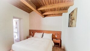 A bedroom with a wooden ceiling, a bed with white linens, two bedside tables, and a nightstand. - Regina 18 (Alleghe)