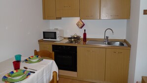 A compact kitchen with wooden cabinets, a microwave, a sink, and a dining table set with colorful plates and cups.