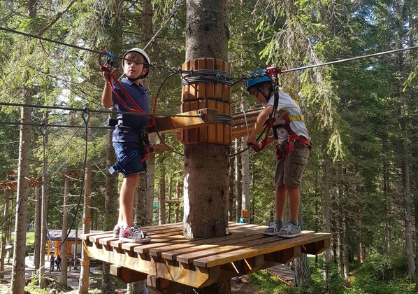 Two people on a wooden platform in a forested area with ropes and safety gear.
