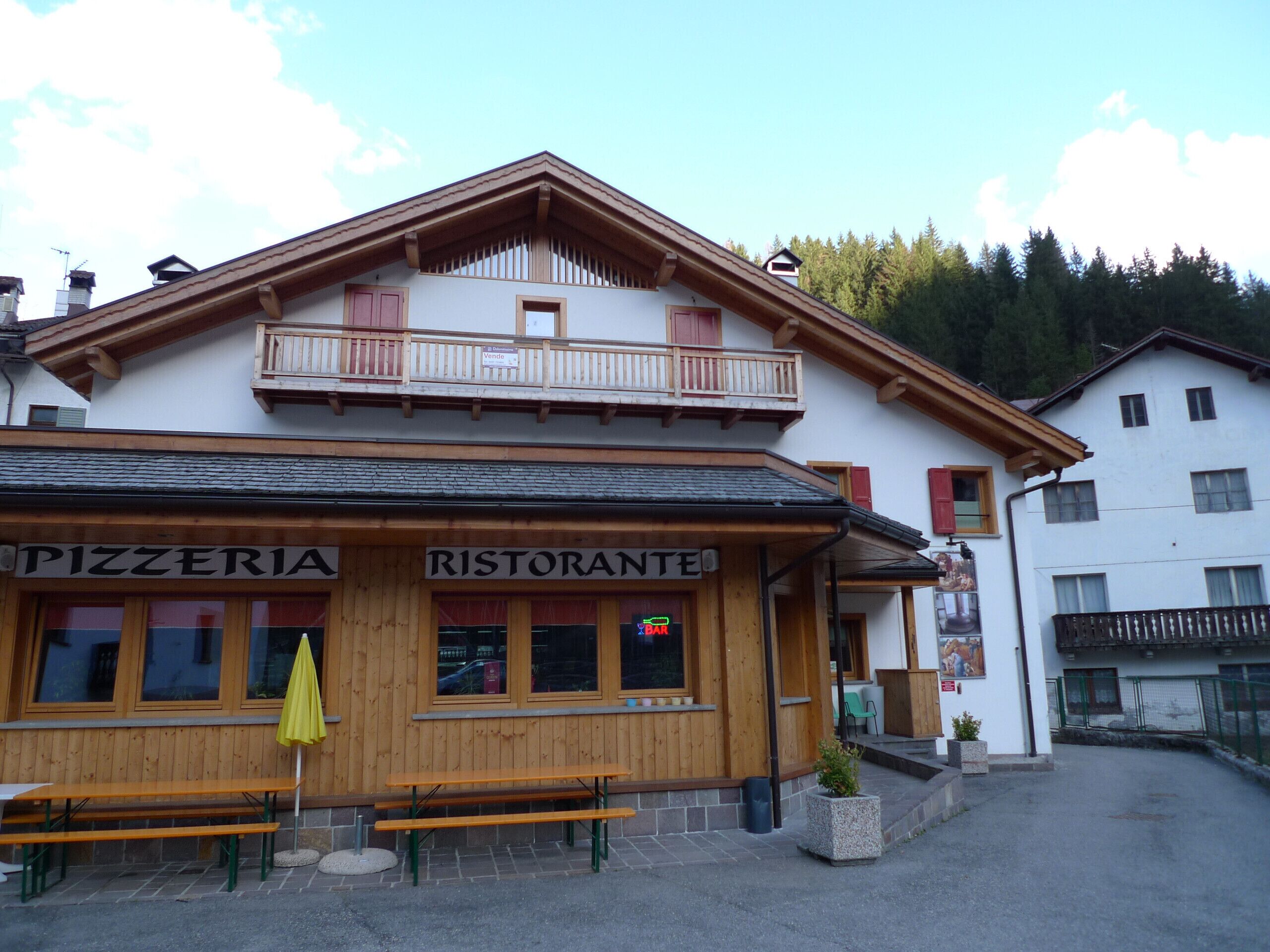 Un bâtiment sur lequel on peut lire l’inscription « PIZZERIA RISTORANTE », et un banc en bois devant l’entrée.
