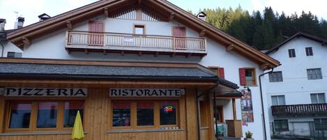 Un bâtiment sur lequel on peut lire l’inscription « PIZZERIA RISTORANTE », et un banc en bois devant l’entrée.