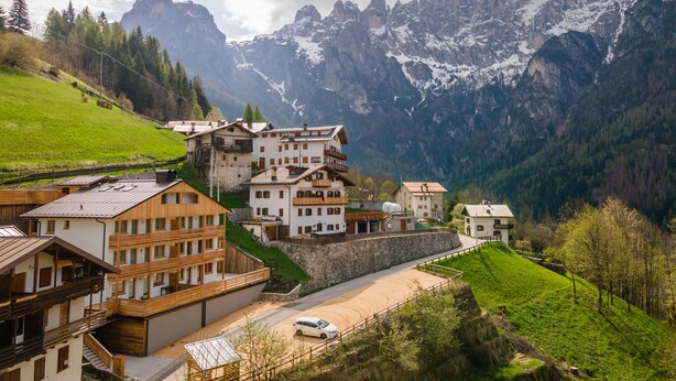 A mountain village with traditional wooden buildings, a paved road, and a car parked in front. - Chalet Laura (Alleghe)