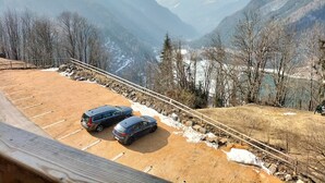 A parking area with two cars, a dirt path, and a view of mountains and a valley. - Chalet Laura (Alleghe)