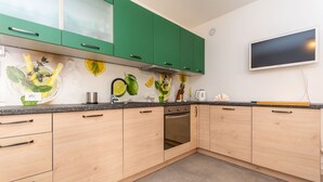 A modern kitchen with green cabinets, a built-in oven, and a backsplash with citrus and herb designs. - Casa Carducci (Alleghe)