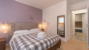 A bedroom with a checkered bedspread, bedside lamps, a mirror, and a wooden floor. - Casa Carducci (Alleghe)