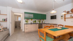 A modern kitchen with green cabinets, a wooden dining table, and a TV mounted on the wall. - Casa Carducci (Alleghe)