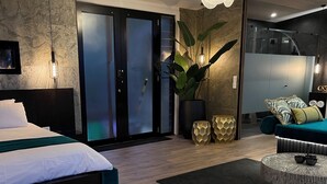 Una habitación de hotel moderna con una cama, una mesa de centro de vidrio, un sofá y una planta grande en maceta.