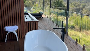 Un baño al aire libre moderno con una bañera blanca grande, un taburete blanco pequeño y un jacuzzi.