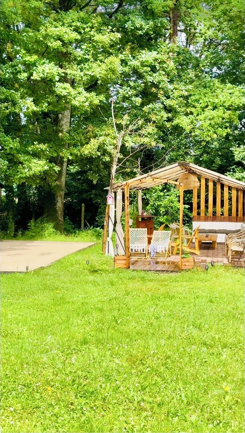 A wooden gazebo with a lattice roof, surrounded by lush green grass and trees.