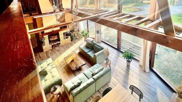 A spacious loft-style living area with a high ceiling, wooden beams, and large windows offering a view of the outdoors. - Chalet Acacia au Calme 1h30 de Paris (La Selle-en-Hermoy)