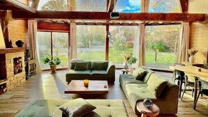 A spacious living room with a high ceiling, large windows, and a fireplace. - Chalet Acacia au Calme 1h30 de Paris (La Selle-en-Hermoy)