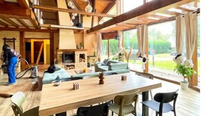 A spacious dining area with a wooden table and chairs, large windows offering a view of the outdoors, and a high ceiling with exposed beams. - Chalet Acacia au Calme 1h30 de Paris (La Selle-en-Hermoy)
