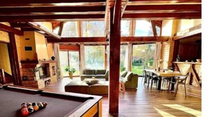 A spacious room with a pool table, wooden flooring, and large windows offering a view of the outdoors. - Chalet Acacia au Calme 1h30 de Paris (La Selle-en-Hermoy)