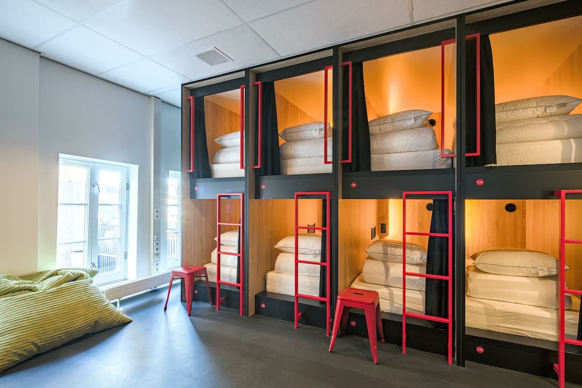 Een slaapzaal met stapelbedden, een raam en een rode trap.