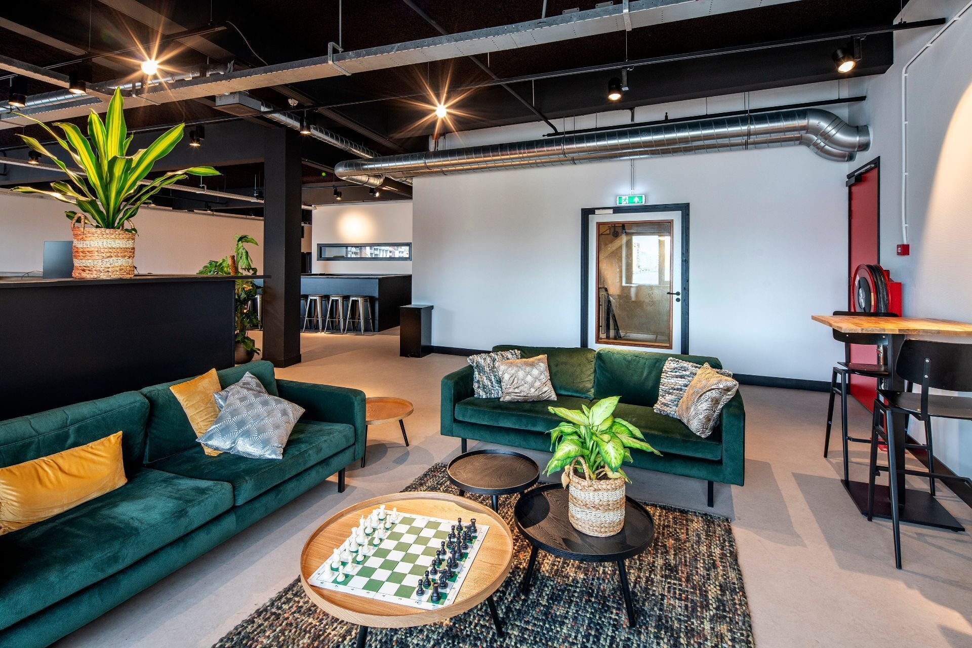 Ein moderner Lounge-Bereich mit grünen Sofas, einem Schachbrett und einer Bar mit Hockern.