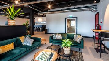Ein moderner Lounge-Bereich mit grünen Sofas, einem Schachbrett und einer Bar mit Hockern.