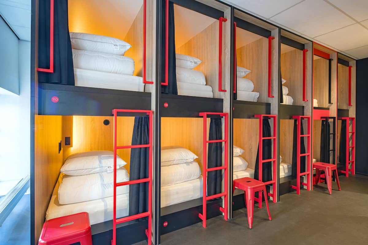 Een hotelkamer met stapelbedden, rode ladders en kleine rode krukjes.