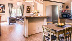 A spacious living area with a wooden ceiling, a dining table with chairs, a kitchen with a refrigerator, and a large window with curtains. - Villa with garden, private pool and air conditioning. Panoramic views!! (Umbria)