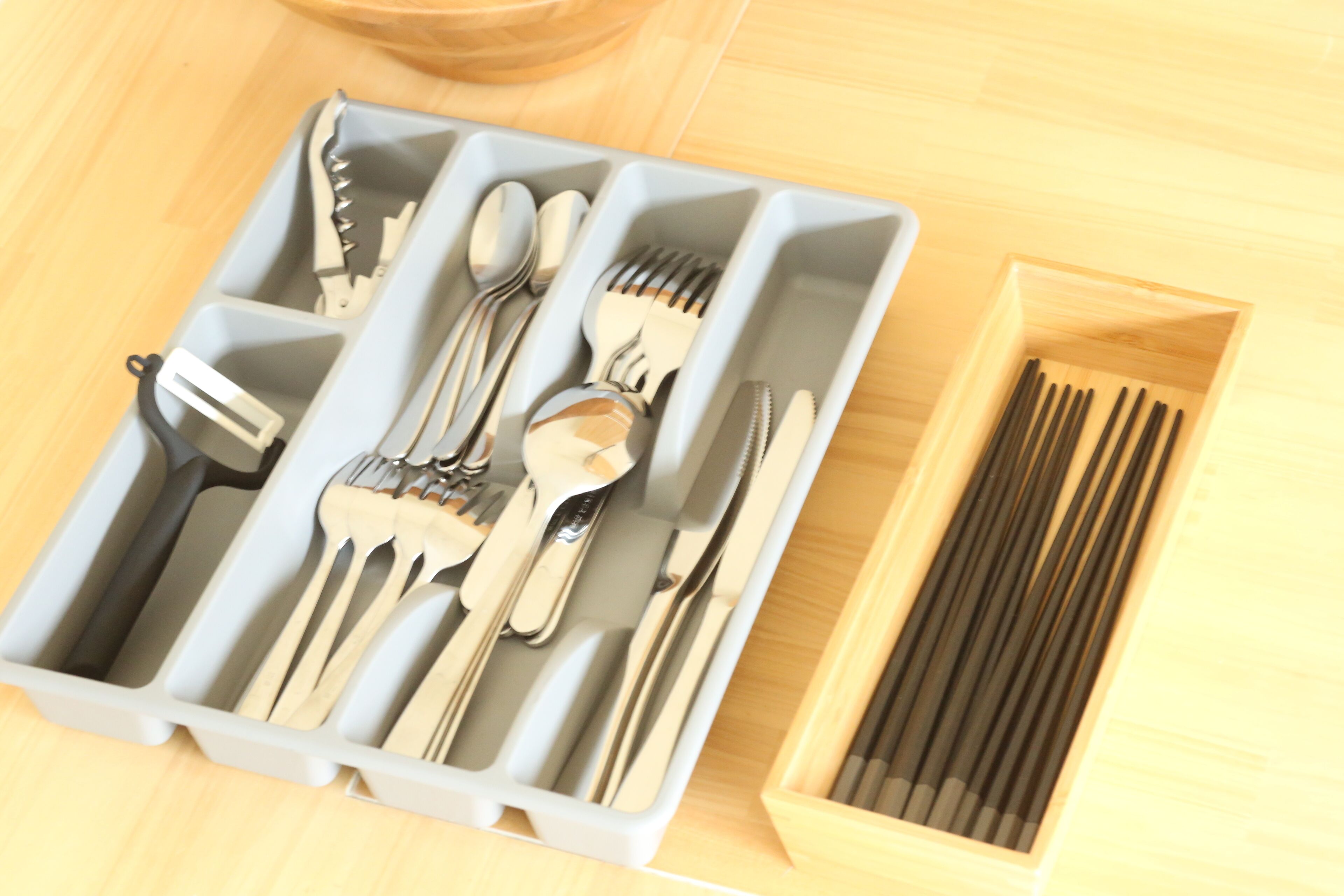 A set of utensils in a gray container, a wooden box with chopsticks, and a wooden surface.