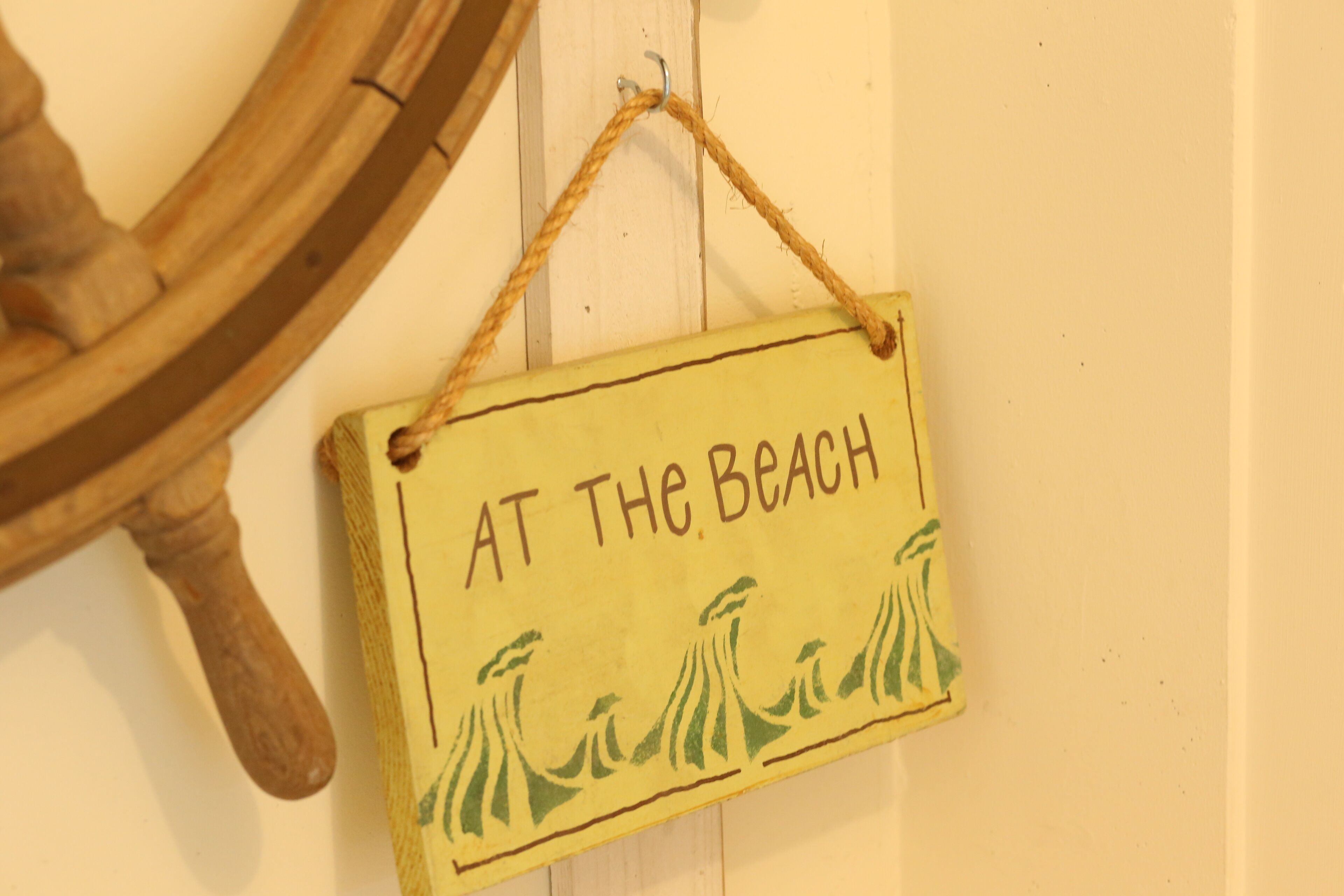 A wooden sign with the text "AT THE BEACH" and a simple illustration of palm trees.