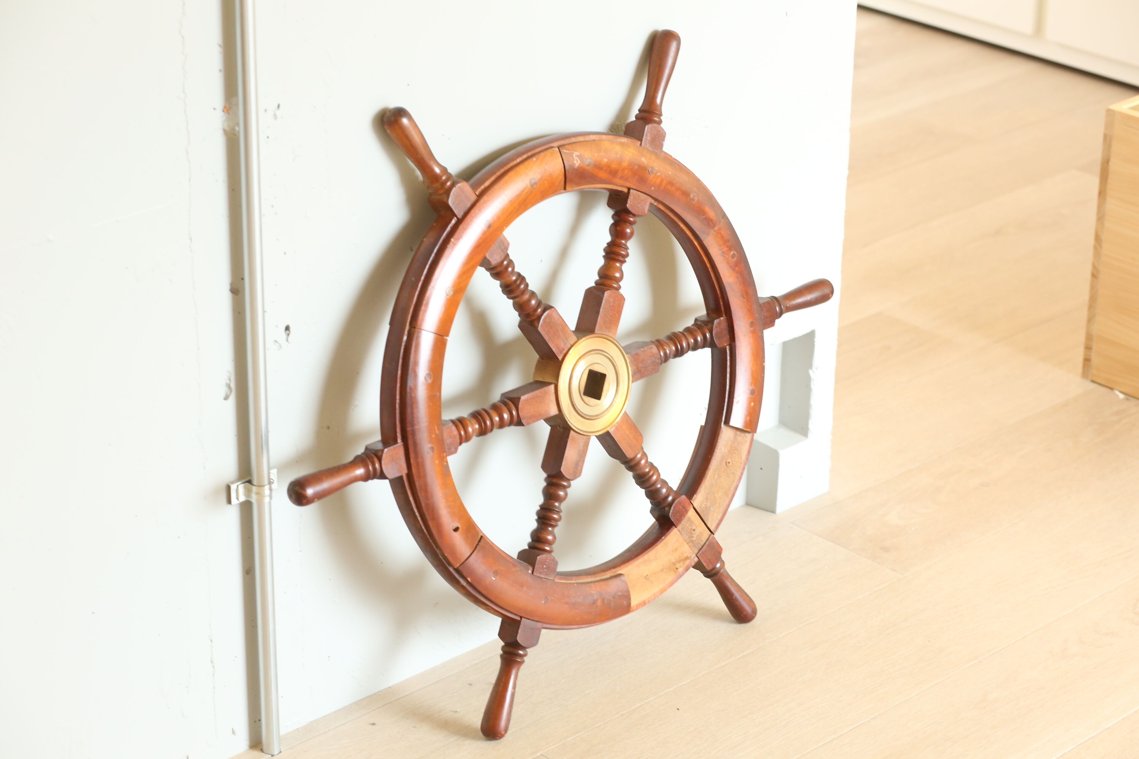 A wooden ship's wheel mounted on a white wall.