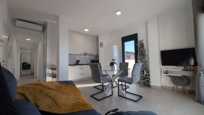 A modern living room with a glass dining table, grey chairs, and a sofa with a mustard throw. A Christmas tree is visible in the background. - Penthouse El Carmelo New, Modernly Furnished with Huge Terrace < 50m from Beach (Caleta de Vélez)