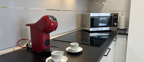 A modern kitchen with a red coffee maker, a microwave, and two cups on a black countertop.